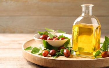 Jojoba seeds in a bowl next to a bottle of jojoba oil.