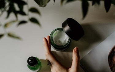 Small pot of cream in a green glass container with foliage at the top of the image