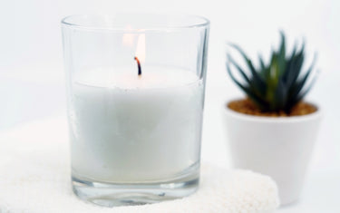 Lit candle in a clear glass jar placed on some towels with a small plant in the background