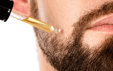 Man applying oil from a pipette onto his beard