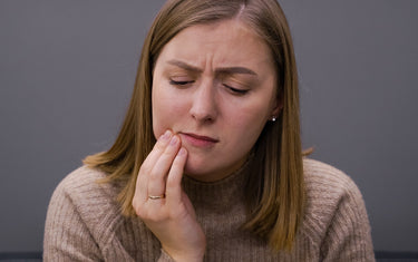 Woman holding side of mouth in discomfort.