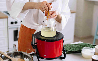 Person melting wax in a beaker over a cooker.