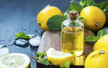 Clear glass vial of lemon essential oil placed on a wooden chopping board with whole lemons and their leaves around it
