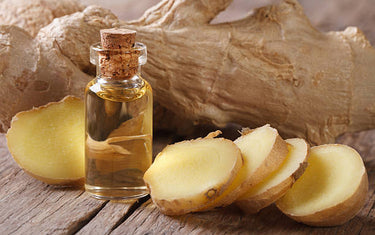 Ginger root part sliced up on a wooden table next to a small clear vial of ginger oil