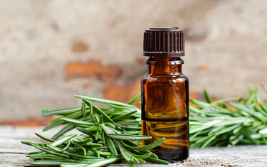 Amber glass bottle next to rosemary oil sprigs