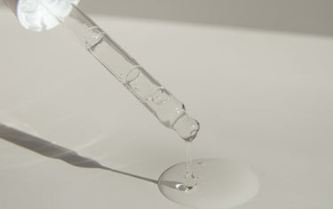 Dropper with colourless liquid on white background.