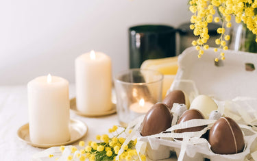 Lit candles, flowers, and small chocolate Easter eggs on the table