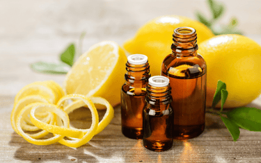 Chopped lemons behind three amber glass bottles filled with lemon oil