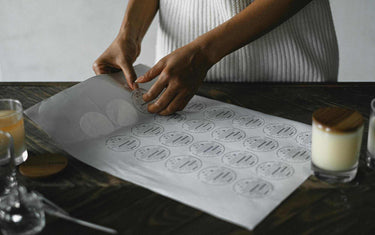 Woman peeling a label off of a sheet of clp labels with a candle placed next to it