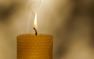 Close up of a thick, lit beeswax candle with a honeycomb texture. Blurred background
