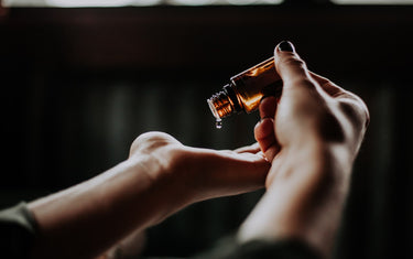 Person dropping oil out of an amber glass bottle into their palm