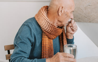 Older person coughing whilst holding a glass of water