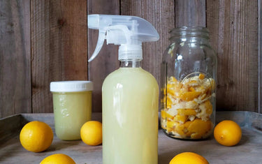 Spray bottle of lemon oil cleaning mixture with a jar of lemon rinds in the background and some lemons scattered around