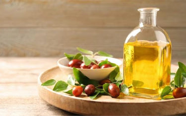 Wooden plate containing a glass jar of jojoba oil, with a small bowl of parts of the jojoba plant