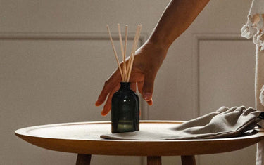 Hand reaching for a reed diffuser on a wooden circular table