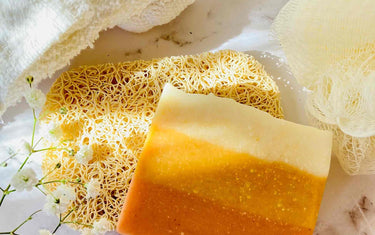 Natural sponge on a marble surface with a block of orange striped homemade soap resting on it.