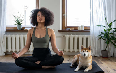 Woman practicing yoga with her dog sat next to her
