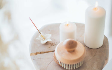 Two white pillar candles on a table with incense and a brush.