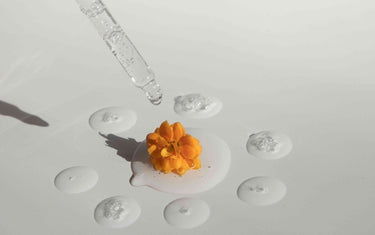 Orange flower in a pool of oil with a dropper.