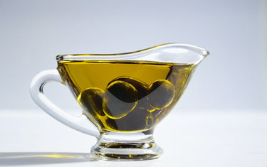 Glass jug of olive oil with black olives in it