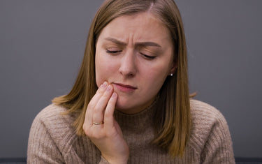 Woman holding side of mouth in discomfort. 