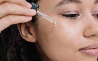 Woman applying oil from a pipette to her face.