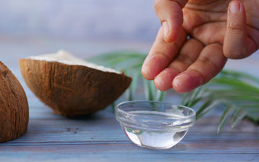 Person scooping coconut oil from dish with raw coconuts in background.
