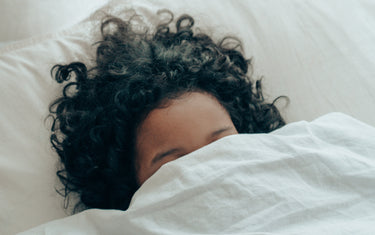 Person asleep in bed with brown frizzy hair.