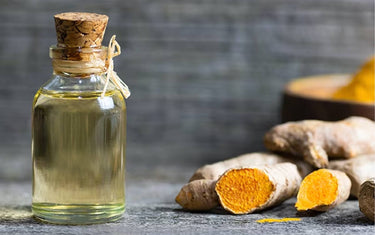 Small clear vial of very light turmeric oil next to chopped up turmeric roots